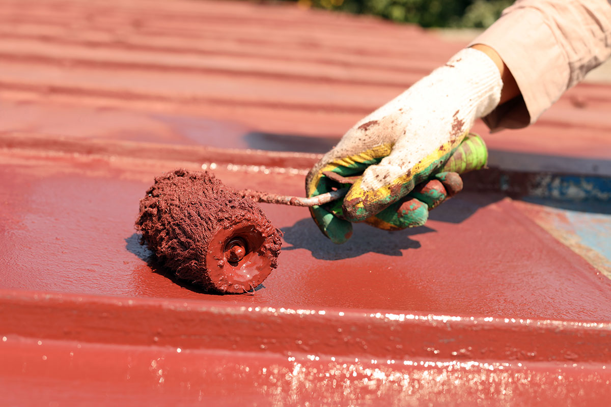 Foto de una mano aplicando pintura sobre una lámina de asbesto