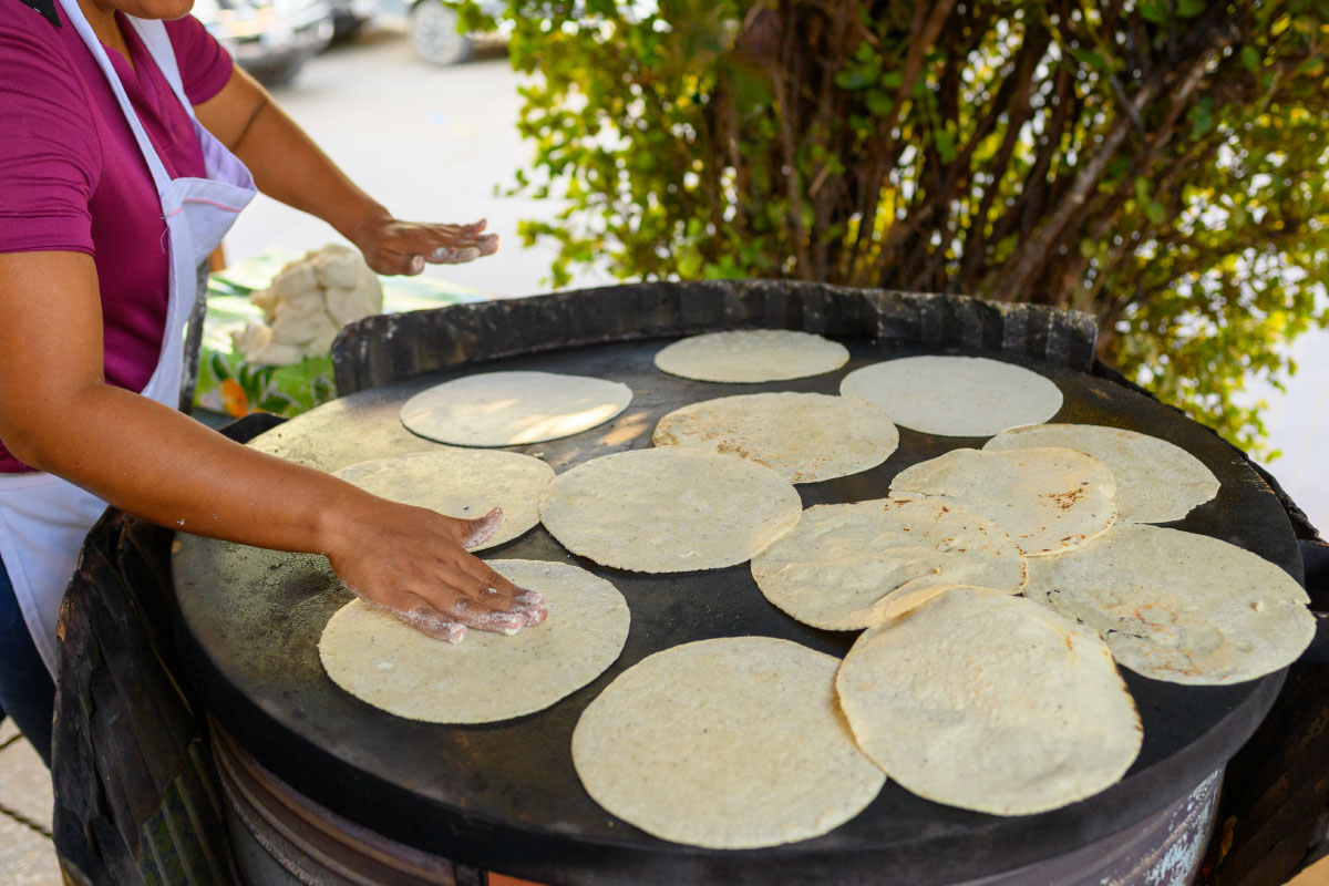 Imagen ilustrativa de una mujer preparando tortillas sobre un comal 